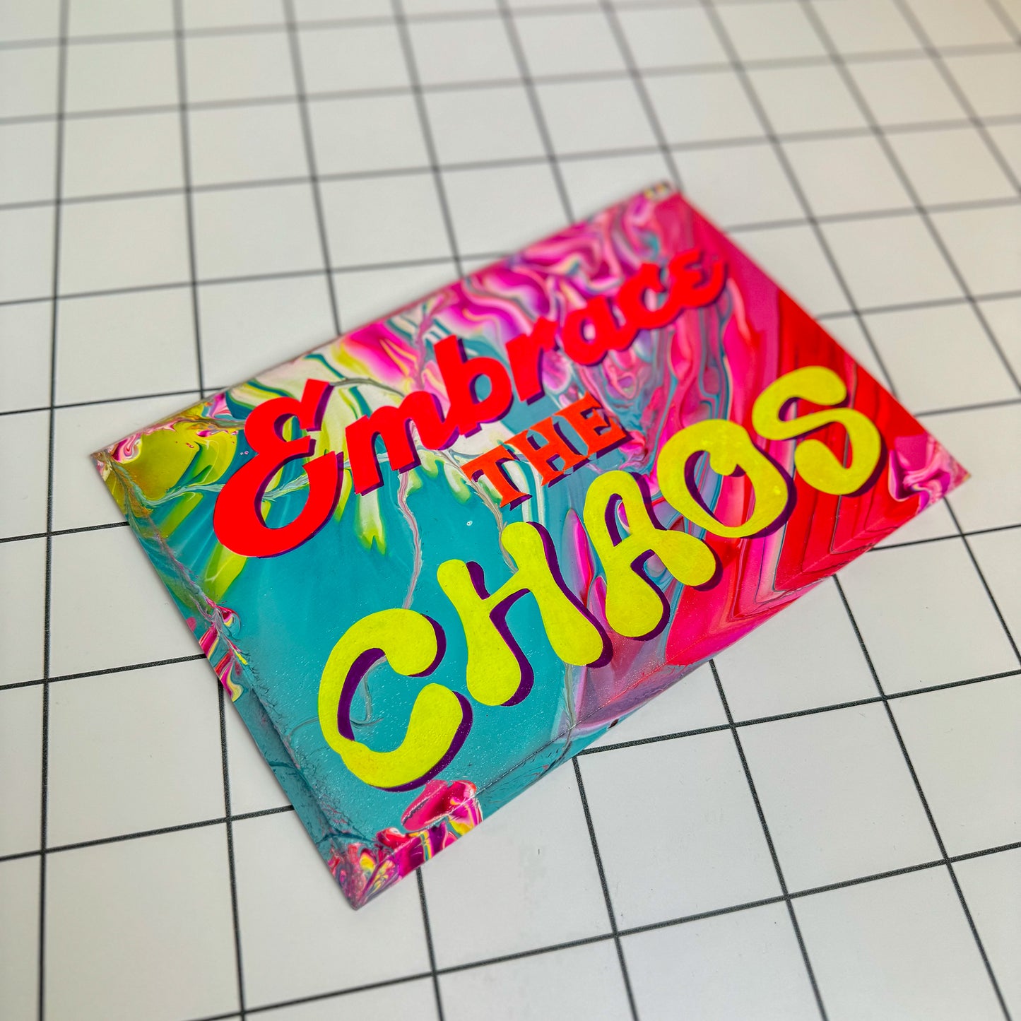 A colourful, hand-painted sign that reads āEmbrace the Chaos,ā designed in a vibrant, maximalist style with foil accents and glossy varnish. A unique gift or statement piece for bold interiors by Stoofy.