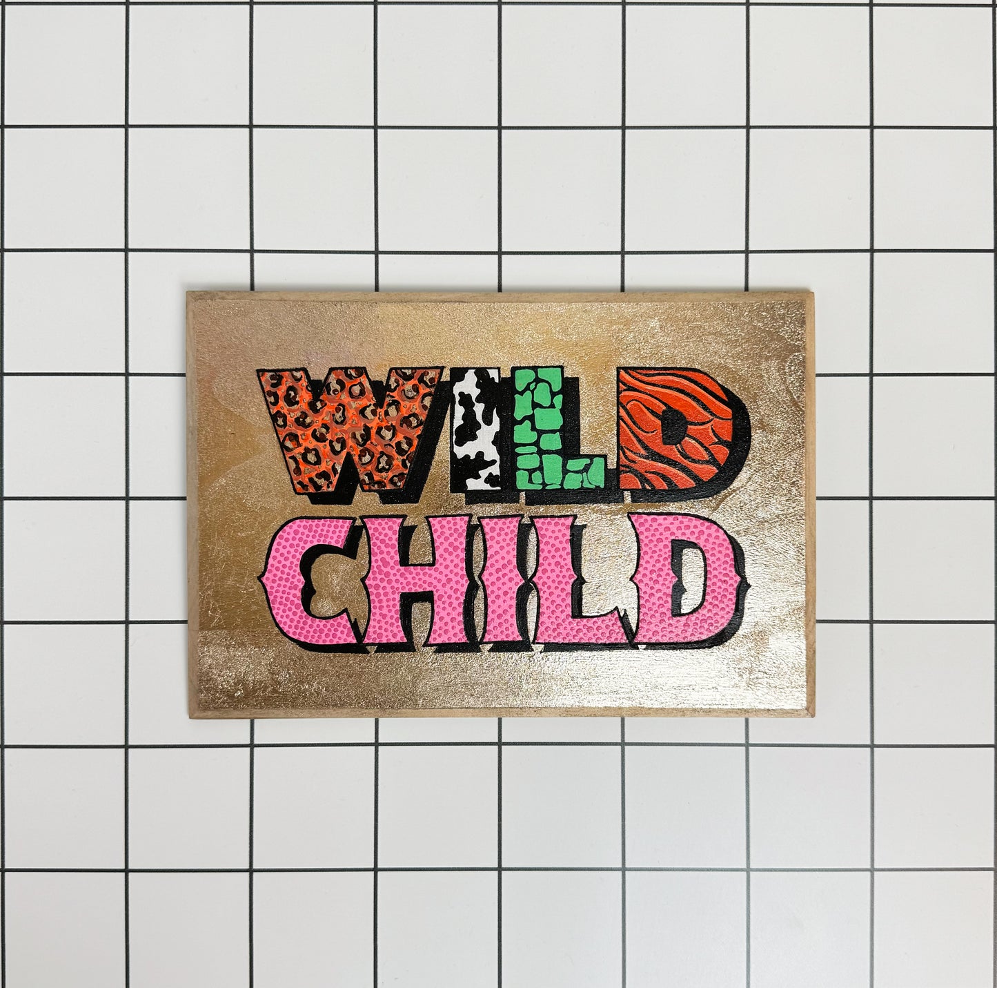 Main image of Stoofy's original hand painted 'Wild Child' sign, gilded with gold metal leaf and bold acrylic lettering on a white background, hand-painted and gloss finished by UK artist, Stoofy. Maximalist interiors.