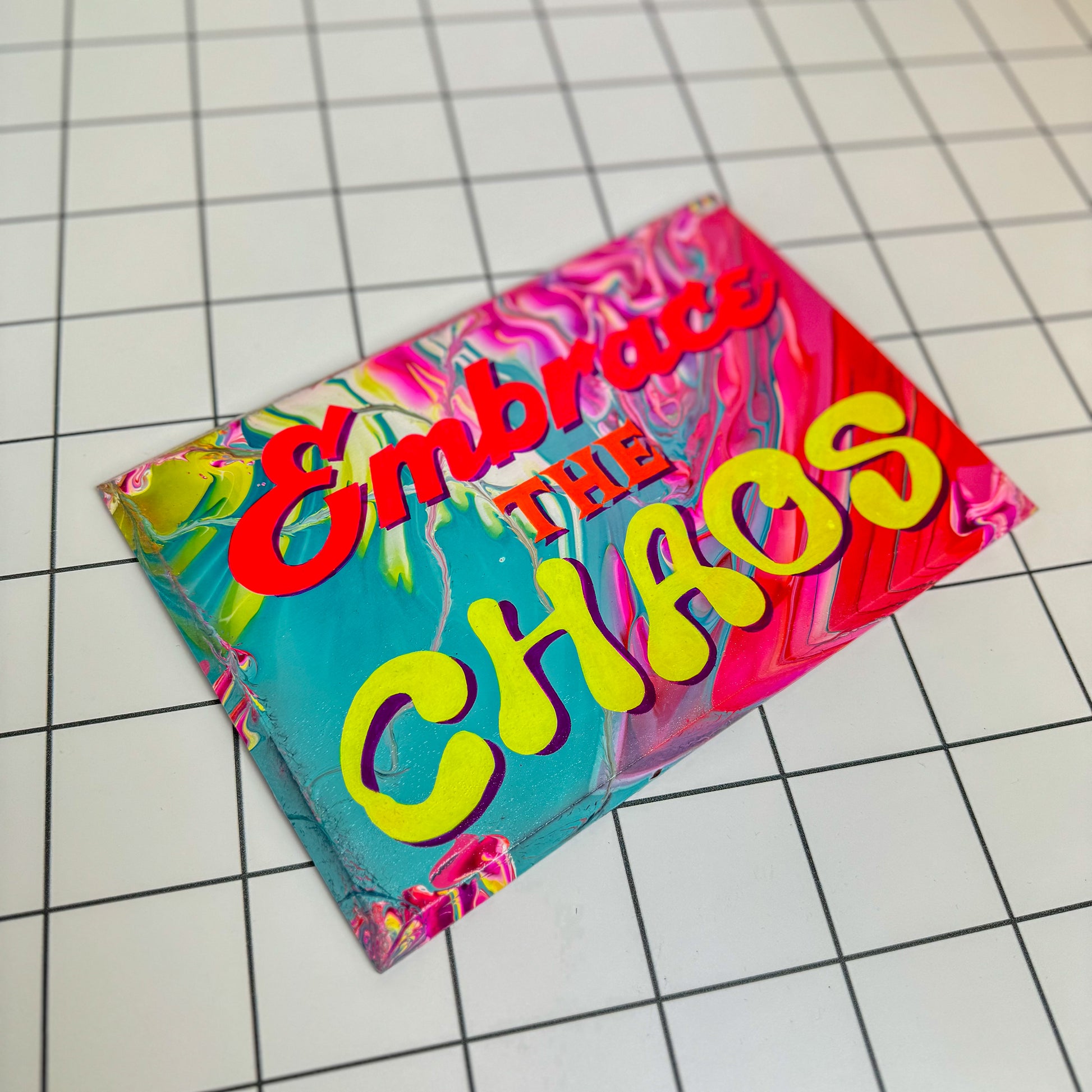 A colourful, hand-painted sign that reads “Embrace the Chaos,” designed in a vibrant, maximalist style with foil accents and glossy varnish. A unique gift or statement piece for bold interiors by Stoofy.