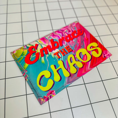 A colourful, hand-painted sign that reads “Embrace the Chaos,” designed in a vibrant, maximalist style with foil accents and glossy varnish. A unique gift or statement piece for bold interiors by Stoofy.