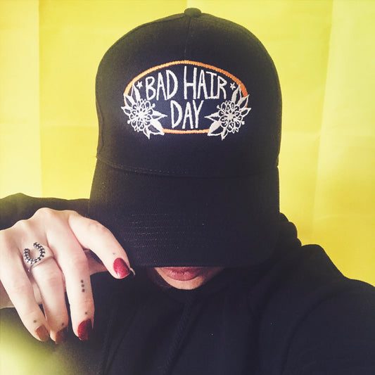 A real person wearing Stoofy's black 6 panel cap with 'BAD HAIR DAY' text and embroidery on the front. Design and copyright owned by UK artist, Stoofy. Perfect for bikers who get helmet hair!